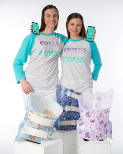 Hadley and Delany holding decorative back braces while holding mobile phones with the BraceTack app installed.